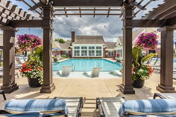 A pool surrounded by a wooden pergola and lounge chairs.